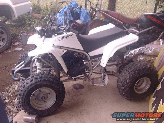 White ATV with YF200 on the side, parked next to a Honda motorcycle and part of a white truck